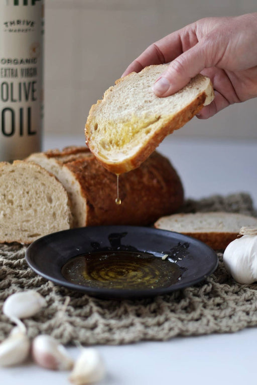 Gravesco Pottery - Garlic Grater Plate in Black: A slice of bread drips olive oil into a textured stoneware plate, ideal for preparing and serving garlicky dips.