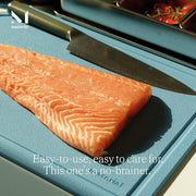 Close-up of Material - The MK Free Board: Cloud with salmon fillet and chef's knife, highlighting its plant-based, non-porous design for safe food preparation.