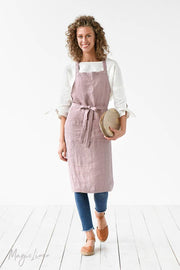 Woman in a pink apron showcasing the MagicLinen - Charcoal Grey Linen Bib Apron with Pockets, highlighting its unisex design suitable for cooking and gardening.