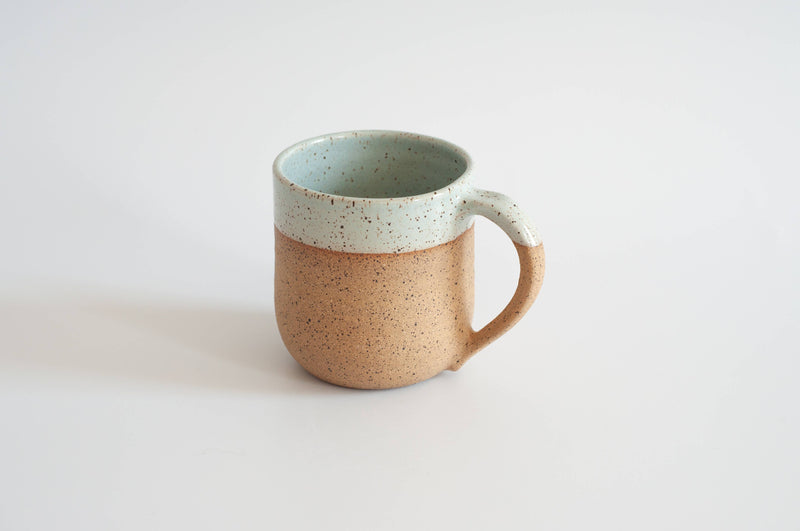 RachaelPots - 12 Oz Original Mug: Sage, hand-thrown ceramic with a thumb rest, featuring a tan base and blue-green glazed rim, perfect for coffee or tea.