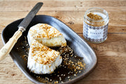 Villa Jerada - Dukkah - 50g: Soft cheese wedge drizzled with honey and dukkah spice blend, served with a vintage knife and open dukkah jar on rustic wood.
