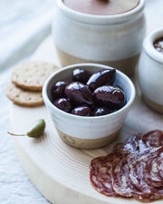 Farmhouse Pottery - Petite Silo Bowl with olives on a wooden board, surrounded by crackers, caperberry, and salami, highlighting its versatile, durable design from Athens Cooks.