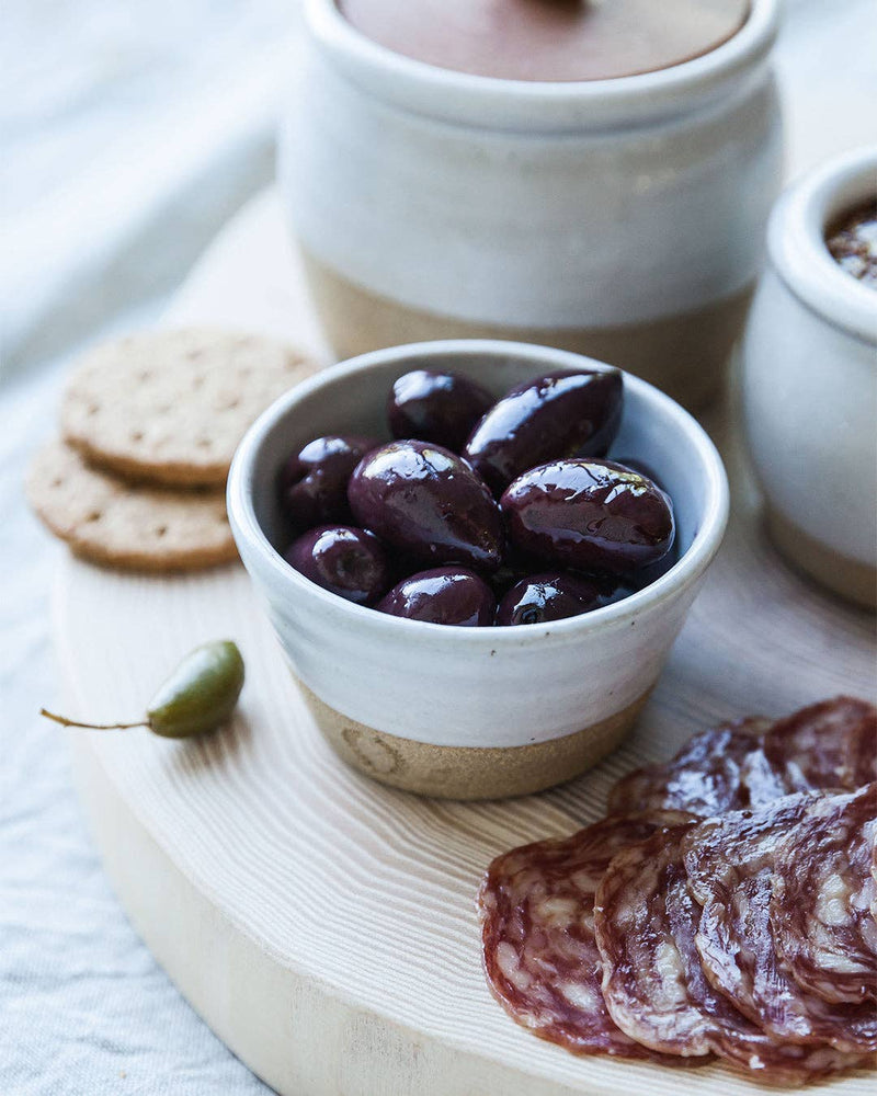 Farmhouse Pottery - Petite Silo Bowl with olives on a wooden board, surrounded by crackers, caperberry, and salami, highlighting its versatile, durable design from Athens Cooks.