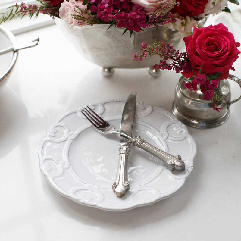 Bella Bianca Antique Lace Salad/Dessert Plate on a table with a fork and knife, next to a vase of flowers.