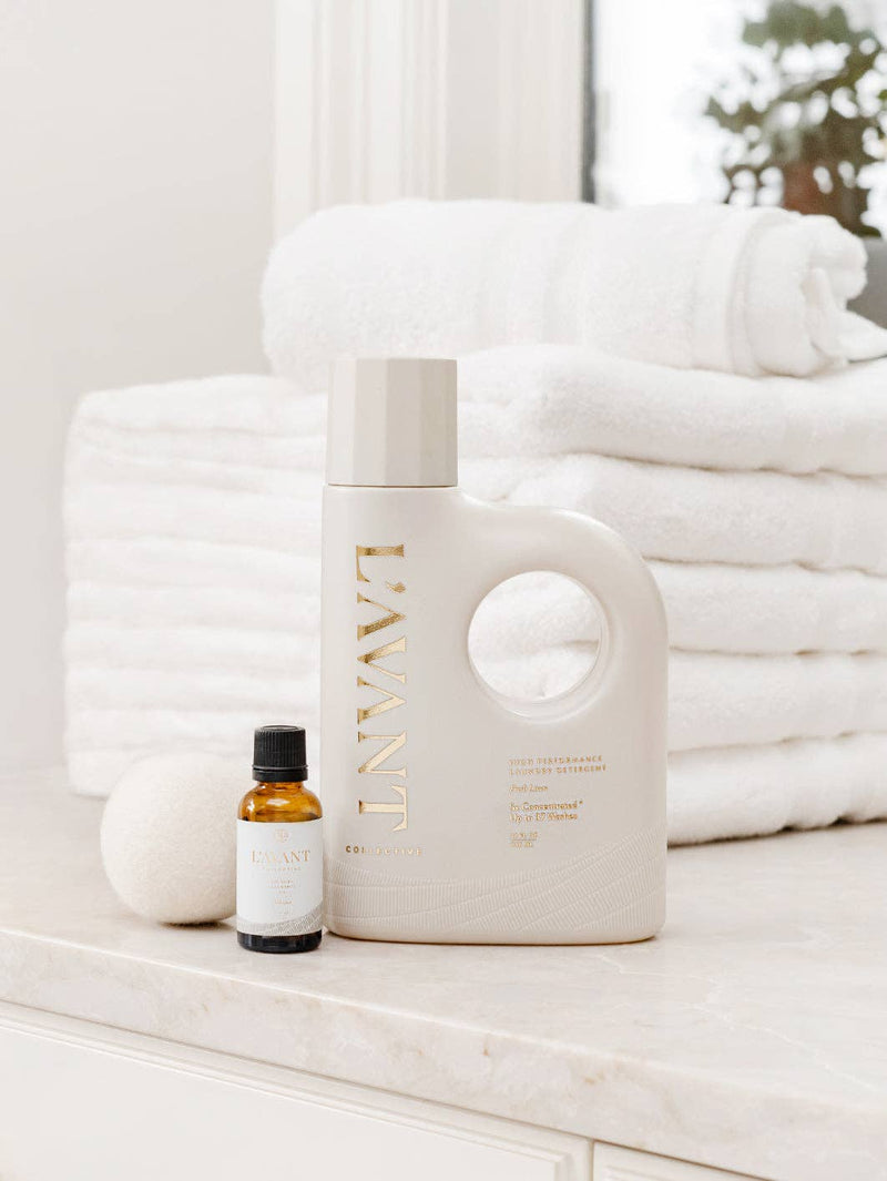 L'AVANT Collective - Laundry Detergent Fresh Linen on a marble countertop with an amber bottle and wool dryer ball, highlighting its eco-friendly, gentle yet effective cleaning formula.