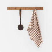 Linen tea towel on rack, featuring a brown and white checkered pattern, made from durable European linen. Perfect for kitchen tasks.