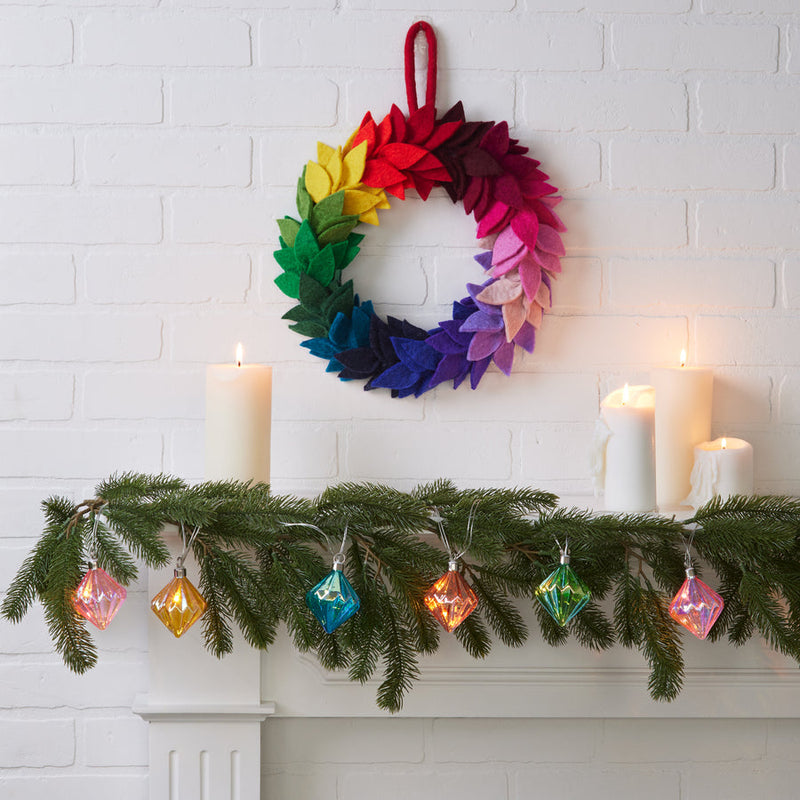 MoMA | LED String Lights Diamond adorn a festive mantel with glowing, faceted ornaments, creating a warm ambiance amid evergreen garland and pillar candles.