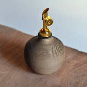 Rose Line Pottery - Oil Bottle - Natural Brown - 14 Ounces sits on wood. Clay vessel with gold misting head, ideal for oil or vinegar.