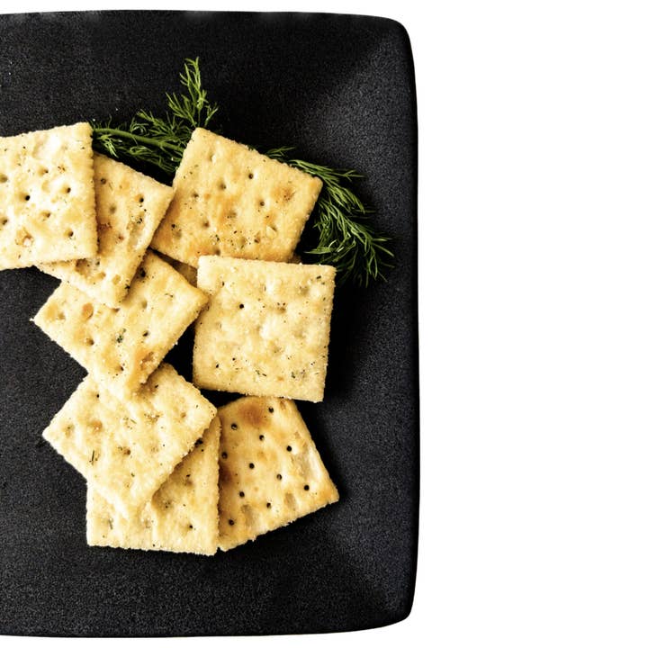 Krackers | Sour Kream and Onion Ranch crackers arranged with a sprig of dill, showcasing their textured surface, embodying classic and modern taste fusion.