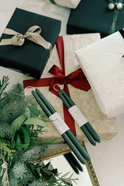 Mo&Co Home - Forest Green Dipped Beeswax Taper Candles placed with festive wrapped gifts and evergreen sprigs, displayed on a reflective gold tray, promoting holiday ambiance.