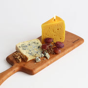 Artifaqt - Blue Cheese Beeswax Candle on a wooden board with grapes, resembling a piece of cheese, showcasing craftsmanship inspired by Birchrun Hills Farm.
