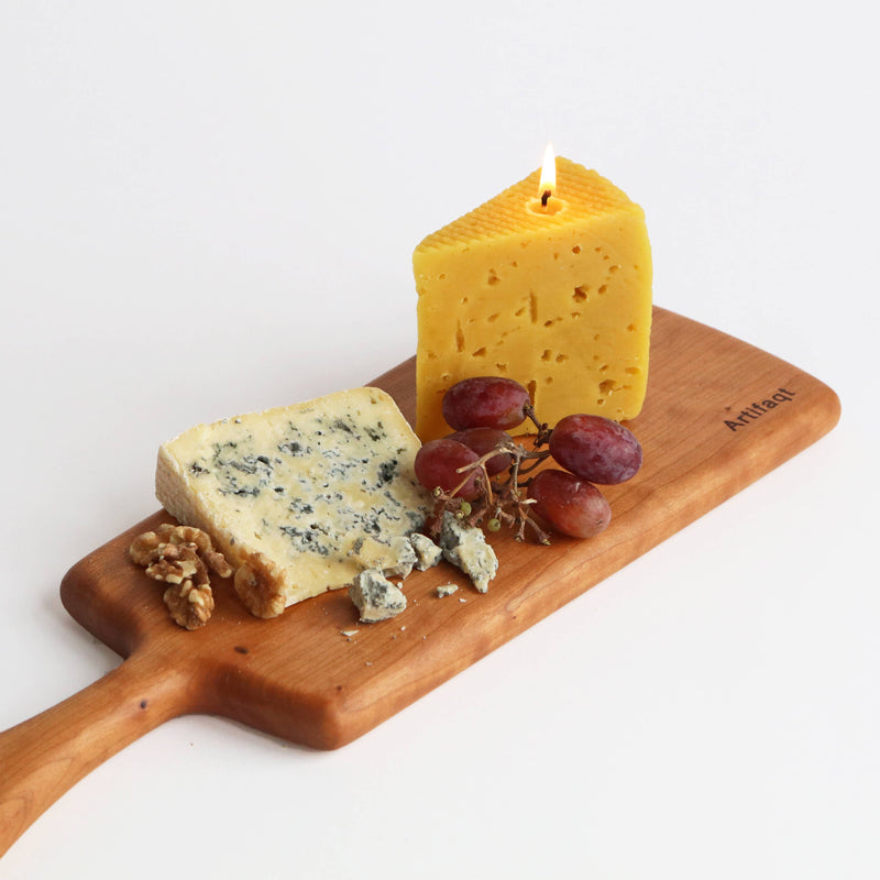 Artifaqt - Blue Cheese Beeswax Candle on a wooden board with grapes, resembling a piece of cheese, showcasing craftsmanship inspired by Birchrun Hills Farm.