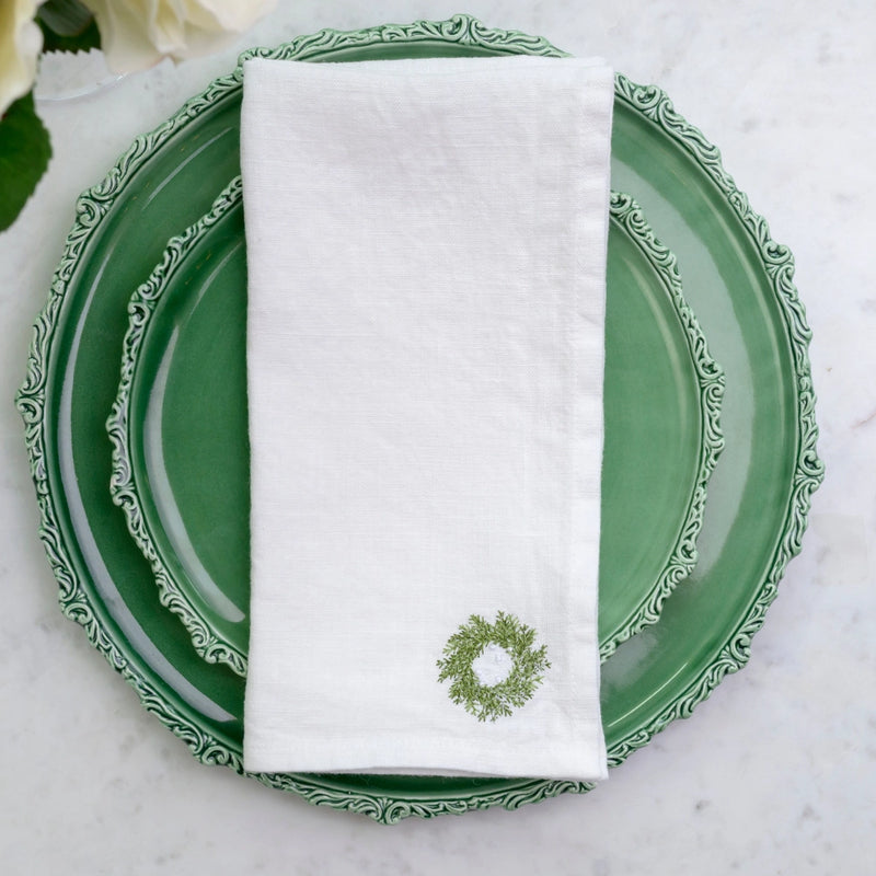 Mini Wreath Napkin Set by Arte Italica & Crown Linen Designs adorns green ceramic plates, adding festive elegance with embroidered linen for holiday dining.