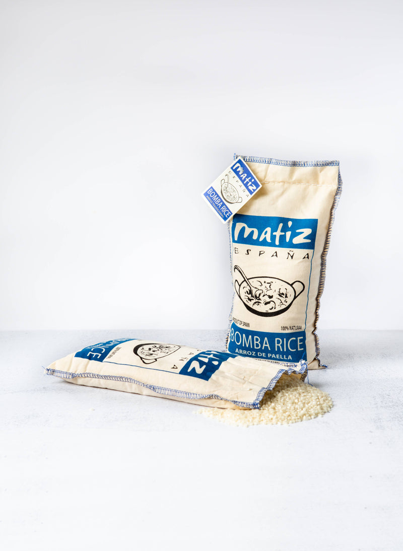 Matiz Bomba Rice 2.2lb bags, one upright and one spilling grains, ideal for flavorful paella, as curated by Athens Cooks kitchen store.