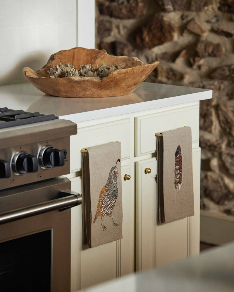 Coral & Tusk - Quail Tea Towel: Detailed quail embroidery on natural linen, hangs from a brass knob in a cozy kitchen scene.