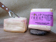 Tulip Tree Creamery - Foxglove cheese being sliced on a cutting board, showcasing its soft texture and distinctive orange rind.