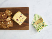 Bee's Wrap - Assorted 3 Pack - Herb Garden, Plant Based Wax shown with cheese on a wooden board, perfect for preserving plant-based foods sustainably.