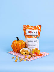 Poppy Hand-Crafted Popcorn - Pumpkin Spice flavor showcased with caramel popcorn, a decorative pumpkin, and cinnamon sticks on a gingham cloth, embodying autumn's essence.