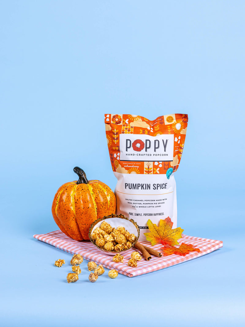 Poppy Hand-Crafted Popcorn - Pumpkin Spice flavor showcased with caramel popcorn, a decorative pumpkin, and cinnamon sticks on a gingham cloth, embodying autumn's essence.