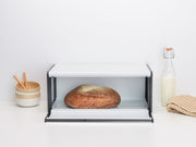 Brabantia USA Inc | Fall Front Bread Box White showcasing its space-saving design with a loaf of bread, ideal for keeping baked goods fresh.
