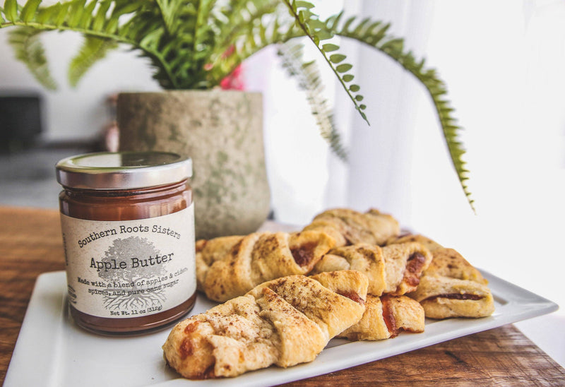 Southern Roots Sisters Apple Butter jar on platter with flaky pastries, showcasing a blend of apples, cider, and spices, perfect for breakfast or snacks.