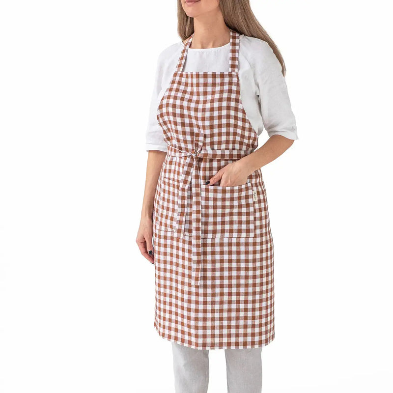 Woman wearing MagicLinen - Charcoal Grey Linen Bib Apron with Pockets, ideal for cooking or gardening, showcasing its checkered pattern and unisex design.