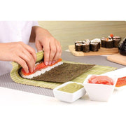 Helen's Asian Kitchen Sushi Mat with Paddle in use, rolling sushi with nori, rice, and salmon. Cutting board with sliced rolls and condiments visible in background.