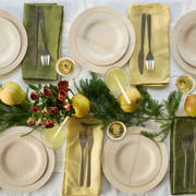 Top-down of festive table setting featuring bambu® Disposable Bamboo Round Plates: 11 inches, with eco-friendly touches like greenery, pears, and matching napkins for a holiday dinner.