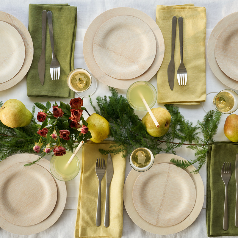 Top-down of festive table setting featuring bambu® Disposable Bamboo Round Plates: 11 inches, with eco-friendly touches like greenery, pears, and matching napkins for a holiday dinner.
