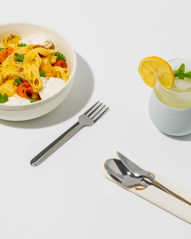 W&P - Stainless Steel Utensils Set in Silicone Carry Case: Terrazzo Charcoal, displayed with a bowl of pasta and a drink, emphasizing portable dining solutions.