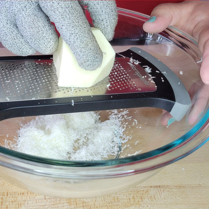 Person grating cheese with Microplane | Bowl Graters, Fine, over a bowl, wearing a cut-resistant glove for safe, efficient kitchen prep.