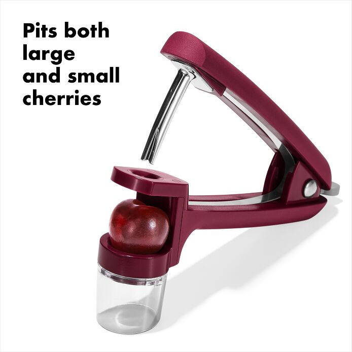 OXO Good Grips Cherry & Olive Pitter in Beet, shown in a plastic container, features a non-slip grip and splatter shield for easy, mess-free pitting.