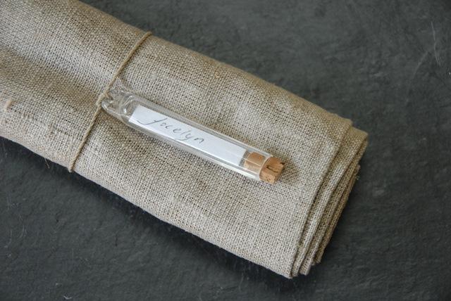 Glass vial with label, designed for use as a unique place marker or decoration, inspired by vintage French plant labels.