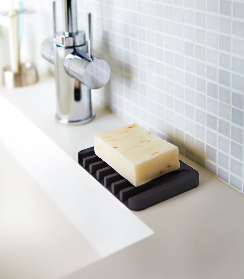 Yamazaki Home | Flow Self-Draining Soap Tray displayed on a bathroom counter, featuring a modern design that keeps soap dry and counters clean.