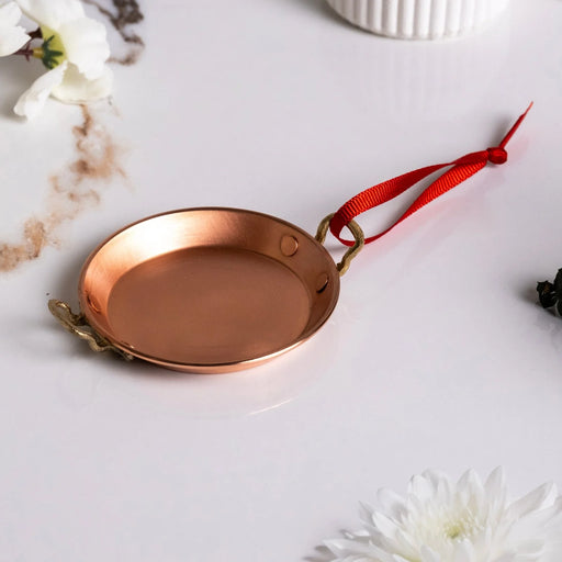 ALFIQ | Handmade Copper Miniature Kitchen Utensil Ornament, Serving Pan with brass handles and red ribbon, displayed with white flowers, capturing old-world charm.