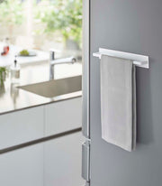 Yamazaki Home | Magnetic Kitchen Towel Hanger, Steel, White, holds a light-gray kitchen towel on a gray refrigerator, enhancing accessibility and organization in a modern kitchen.