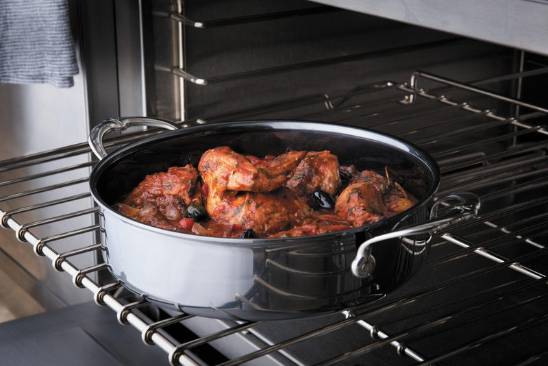Hestan | NanoBond Cookware, 3.5qt Sauteuse on oven rack, braising chicken in tomato sauce with olives, showcasing its superior heat conduction and scratch-resistant surface.