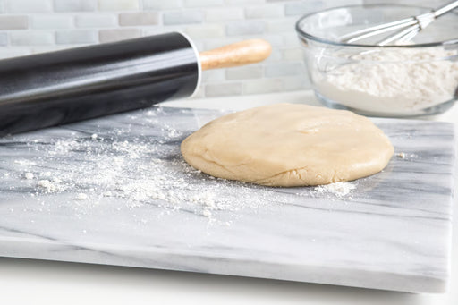 Marble Pastry Board, White: Rolled-out dough on a marble board, with a rolling pin and mixing bowl in the background, suggesting baking preparation.