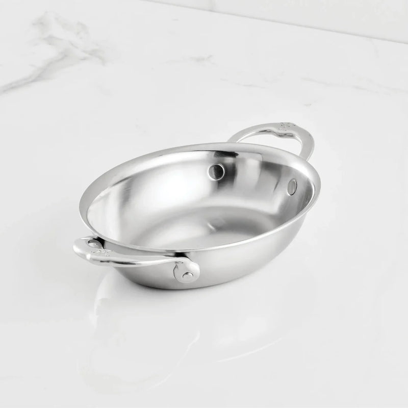 Hestan Provisions | Chef's Special Oval Clad Au Gratin: A polished stainless-steel pan with loop handles, ideal for cooking or serving, on a white countertop.