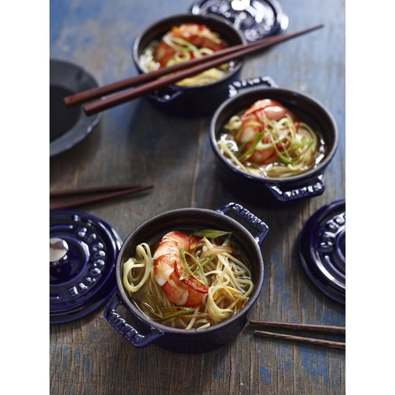 Staub | Mini Round Dutch Oven, Dark Blue, 0.25 QT, filled with noodle soup and shrimp, garnished with scallions. Chopsticks rest on top, set on wooden surface.