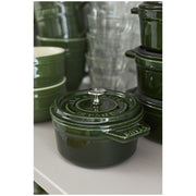 Staub Mini Round Dutch Oven in basil green, 0.25 QT, on a shelf; perfect for single-serve dishes, featuring a self-basting lid and scratch-resistant interior.