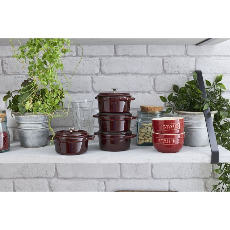 Staub | Mini Round Dutch Oven, Grenadine, 0.25 QT., showcased on a white shelf with maroon-red cocottes, glass jars, and trailing houseplants, highlighting its compact elegance.