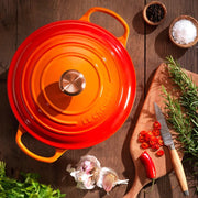 Le Creuset | Signature Round Wide Oven - Flame, surrounded by chili slices, garlic, rosemary, herbs, and spices on wooden table, showcasing vibrant design and versatility.