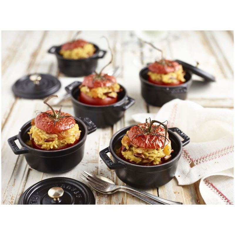 Staub Mini Round Dutch Oven, Black, 0.275 QT., featuring a hollowed tomato with yellow rice, displayed with a fork and napkin on a wooden surface.