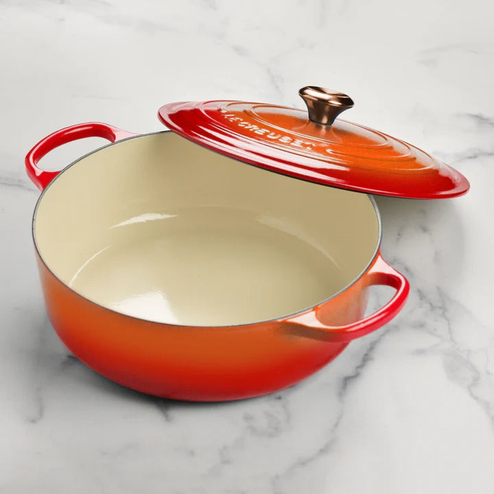 Le Creuset Signature Round Wide Oven in Flame on marble countertop, showcasing its enameled cast iron build and bronze knob, ideal for versatile cooking and elegant presentation.