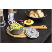 Staub Mini Round Dutch Oven, Graphite, 0.275 QT., filled with guacamole, on a wooden board with avocado, onion rings, and bread slices nearby.