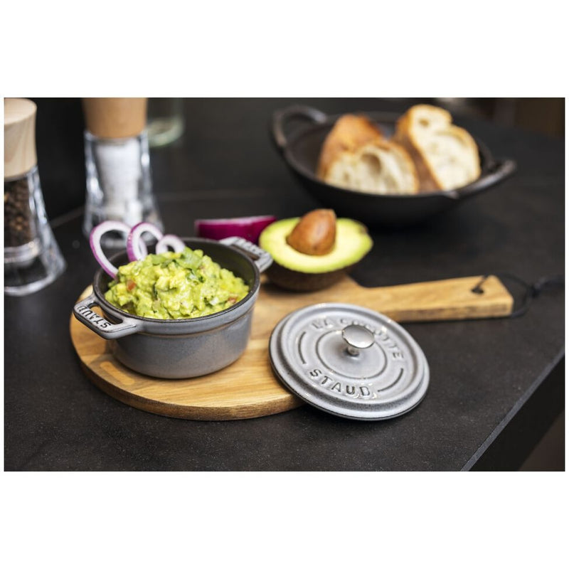 Staub Mini Round Dutch Oven, Graphite, 0.275 QT., filled with guacamole, on a wooden board with avocado, onion rings, and bread slices nearby.