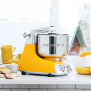 Ankarsrum stand mixer in a kitchen scene with bread and citrus juicer, embodying Athens Cooks' focus on quality, versatile kitchen tools for baking and cooking.