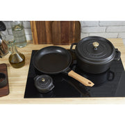 Staub | Mini Round Dutch Oven, Black, 0.275 QT., sits on a black induction cooktop, surrounded by Staub cookware and kitchen essentials on a wooden countertop.