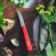Opinel | Essential Birdsbeak Vegetable Knife - Pink with a red handle on a cutting board, surrounded by artichoke pieces, fennel flowers, and a folded green napkin.